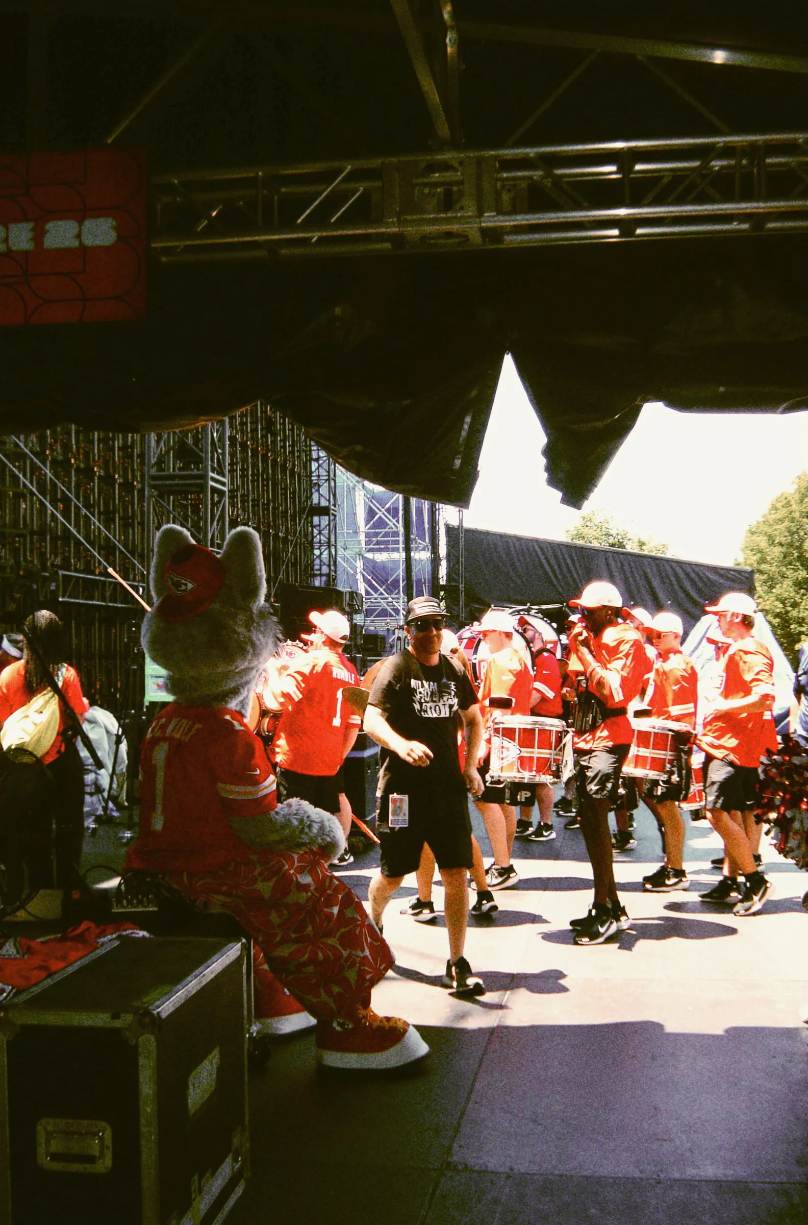 A drumline in red and white playing under the stage truss, shot from the wings