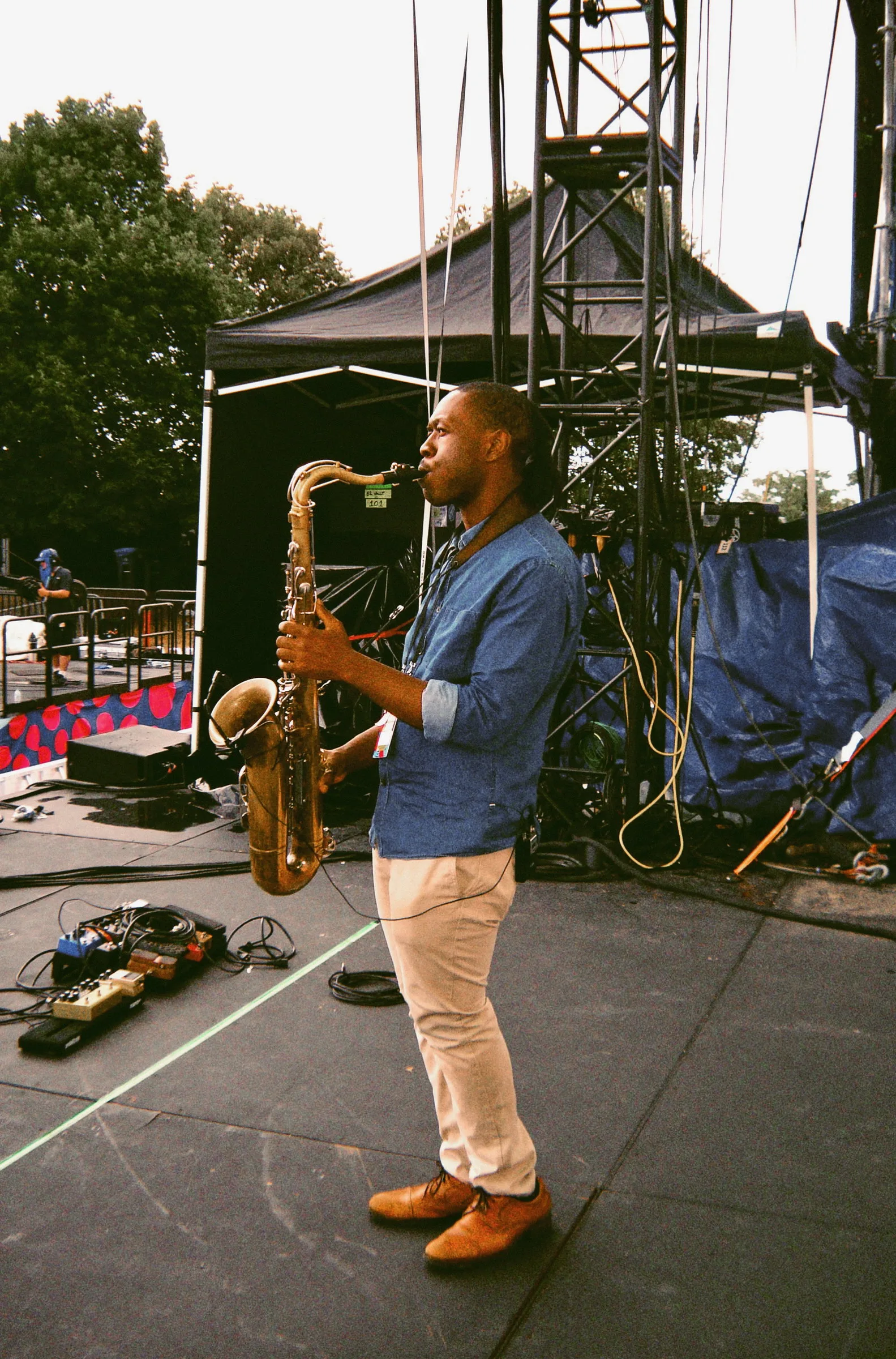 A saxophonist playing on a wide empty stage surrounded by cables, stands and rigging