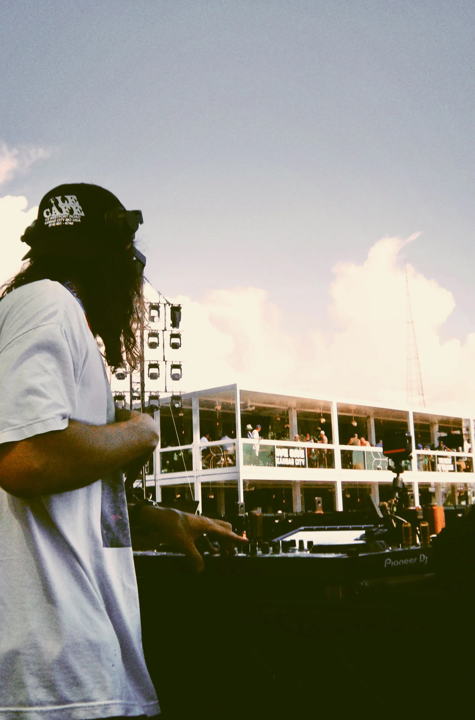 A DJ working at the decks, framed against an open sky and the venue structure behind