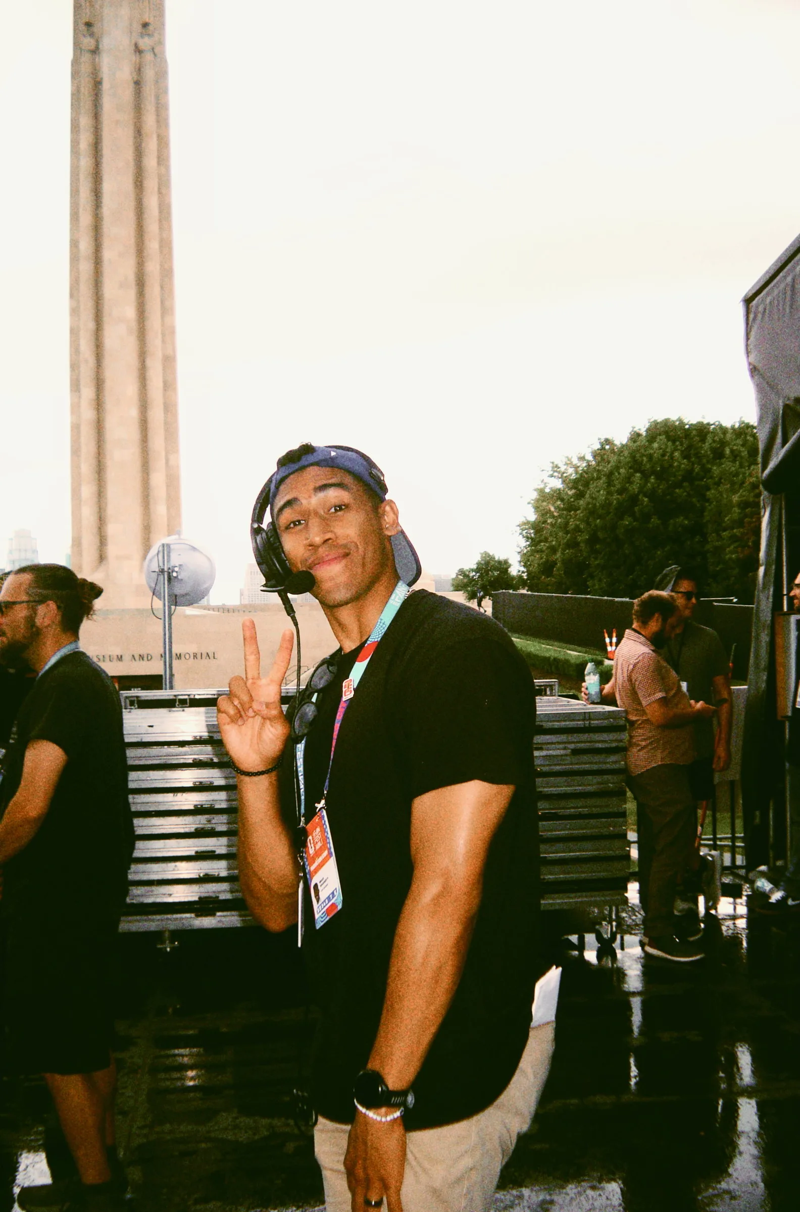A crew member in a lanyard turning to the camera and throwing a peace sign