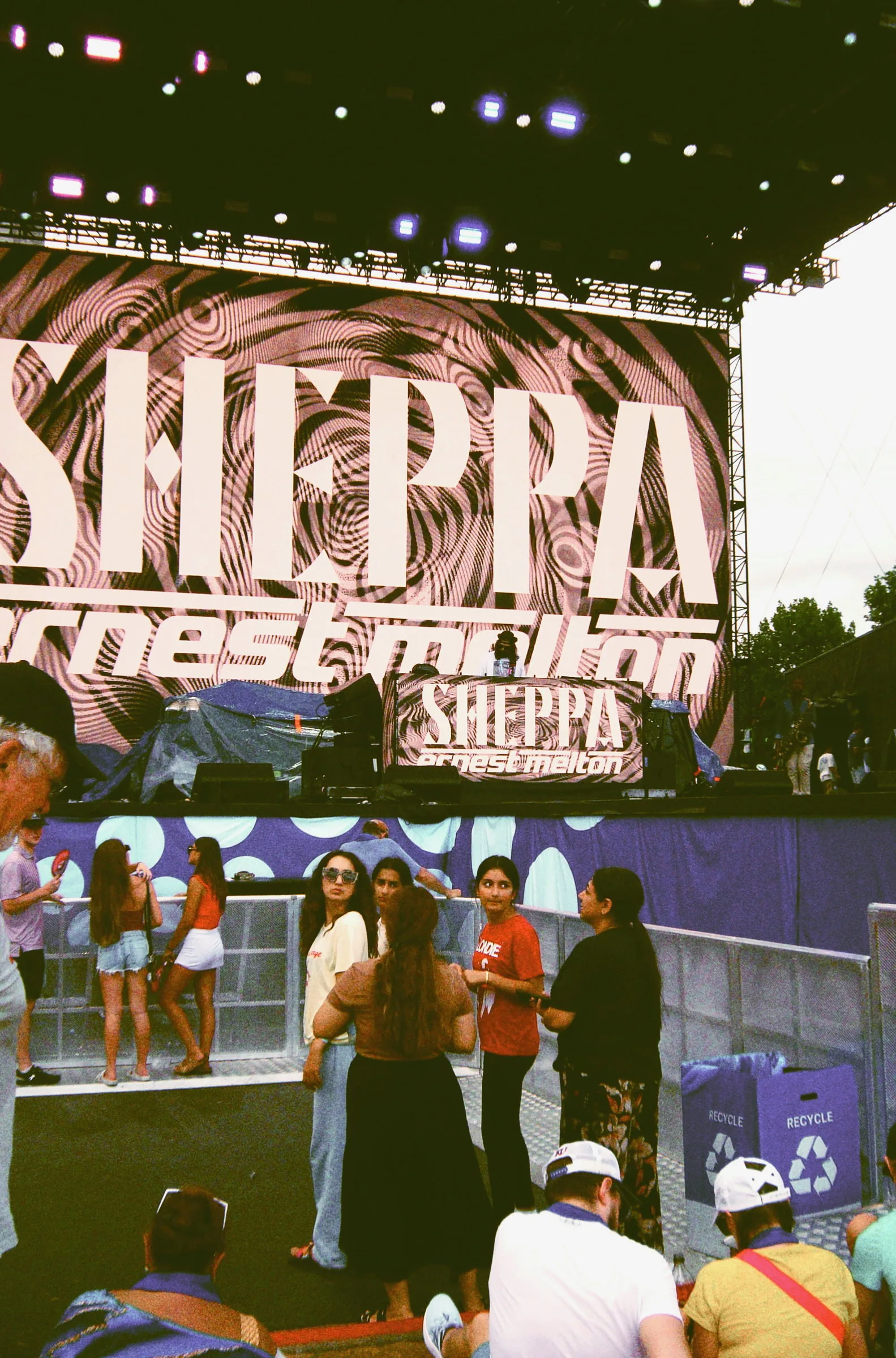 The main stage seen from the crowd, screens lit up above people milling in the fan zone