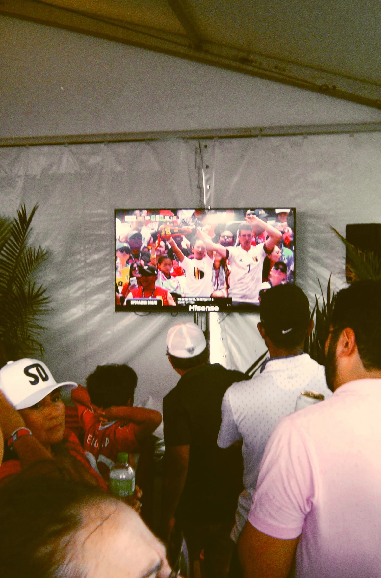 People crowded around a television inside a marquee, watching a match